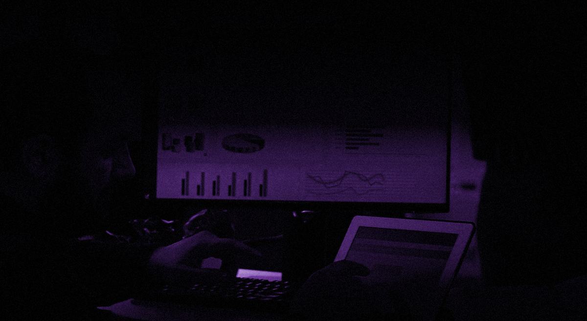 Profissional analisando painéis de indicadores em duas telas, no escuro